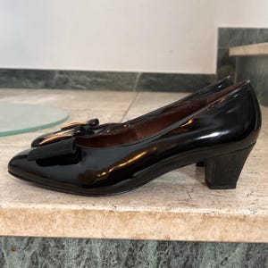 Può includere: Pumps in vernice nera con fibbia dorata e tacco basso a blocco.