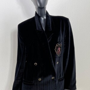 Peut inclure: Veste blazer noire en velours à double boutonnage avec boutons dorés et écusson brodé. La veste est associée à une casquette à motifs. La veste présente un design texturé et côtelé.