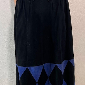 May include: Black suede skirt with a blue suede belt and a blue and black diamond pattern at the hem. The skirt has a high waist and a midi length. The belt has a square buckle.