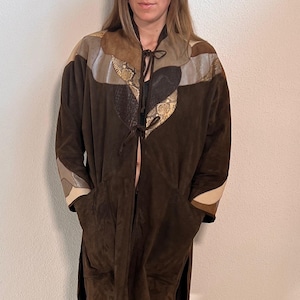 Könnte beinhalten: Ein brauner Wildledermantel mit Patchwork-Details, mit Akzenten in Beige, Grau und Schlangenmuster. Der Mantel hat einen Bindverschluss und Taschen. Eine Cordkappe mit Seildetail rundet den Look ab.
