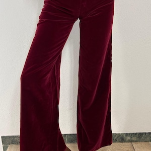 Könnte beinhalten: Bordeauxfarbene Samthose mit weitem Bein. Die Hose hat eine hohe Taille und eine weiche, fließende Textur. Die Hose wird mit Plateausandalen kombiniert.