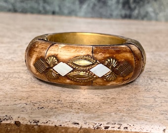May include: A brown and gold bangle bracelet with white shell inlays. The bracelet is made of wood and metal.