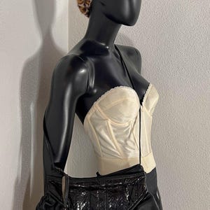 Pode incluir: Uma bolsa de ombro de couro preta com aba de pele de cobra e borla. A bolsa é combinada com um espartilho creme e uma boina com estampa de leopardo. O manequim é preto.
