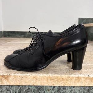 May include: Black leather lace-up shoes with a rounded toe and a chunky heel. The shoes have a classic design with a lace-up closure and a sturdy heel, suitable for various occasions.