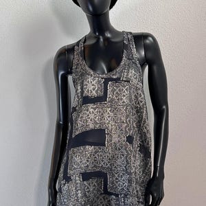 May include: A sleeveless silver and black dress with a geometric pattern is displayed on a black mannequin. The dress has a scoop neck and a loose fit. A black fur hat is on the mannequin's head.