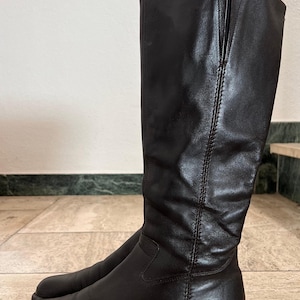 May include: A pair of knee-high, dark brown leather boots. The boots have a rounded toe, a low heel, and a vertical seam down the front. The leather appears smooth and slightly worn, suggesting a vintage style.