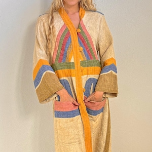 May include: A long-sleeved, beige textured coat featuring a vibrant, multi-colored geometric pattern in shades of orange, blue, green, and pink. The coat includes a solid orange front placket with buttons, two large front pockets, and a matching beige bucket hat.