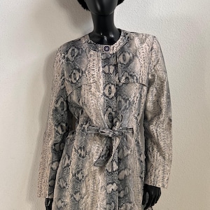 May include: A long-sleeved coat featuring a grey and black snakeskin pattern, a round neckline with a single button closure, and a matching tie belt at the waist. The coat is displayed on a mannequin wearing a black faux fur hat.