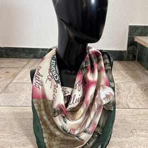 Könnte beinhalten: Ein grüner, rosa und weißer Seidenschal mit einem gewebten Muster und dem aufgedruckten Text "ATHENES" und "GALLINO".
