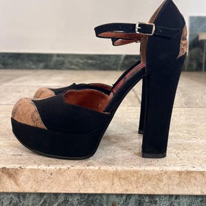 May include: Black platform heels with a cork-like texture on the toe and heel. The shoes have a thick, block heel and a strap that buckles around the ankle. The interior is red.