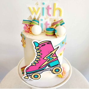 Peut inclure: Un gâteau blanc décoré de vermicelles colorés, de bonbons et d'un graphique de patins à roulettes. Le gâteau est surmonté d'une pancarte qui dit "roll with it".