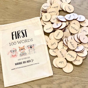 May include: A white canvas bag with the words "FIRST 100 WORDS" printed on it. The bag contains 100 wooden circles with different words written on them. The bag is suitable for ages 3 and up.