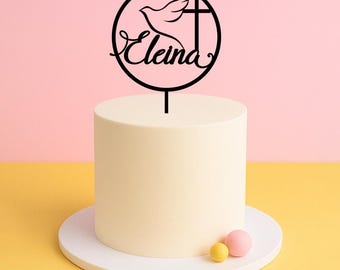 May include: Black cake topper with a white dove and cross design. The topper is in a circle with the name "Eleina" written in cursive.