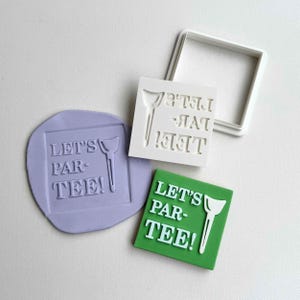 Puede incluir: Un conjunto de cortadores e impresiones de galletas con temática de golf. El diseño incluye el texto "LET'S PAR-TEE!" con un gráfico de tee de golf. Una impresión está en un cuadrado verde, otra en un círculo morado y un cortador blanco.