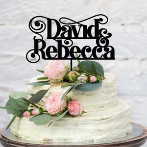以下が含まれることがあります： 装飾的な書体で「David & Rebecca」と書かれた黒いアクリル製のケーキトッパーです。