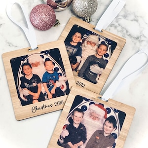 May include: Three wooden ornaments with photos of children with Santa Claus. Each ornament has a white ribbon for hanging and the year printed on the bottom. The ornaments read "Christmas 2009", "Christmas 2010", and "2012".