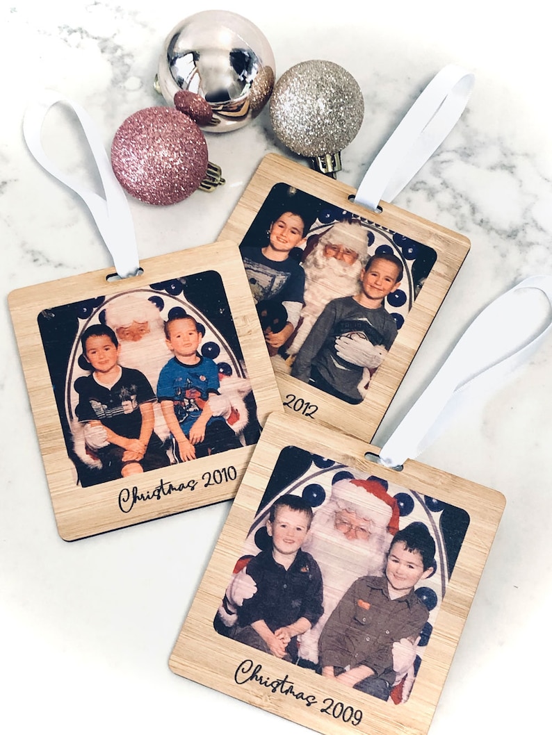 May include: Three wooden ornaments with photos of children with Santa Claus. Each ornament has a white ribbon for hanging and the year printed on the bottom. The ornaments read "Christmas 2009", "Christmas 2010", and "2012".