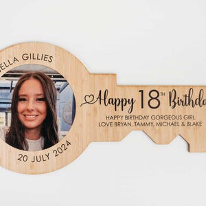 Może przedstawiać: Drewniana ramka na zdjęcia w kształcie klucza z fotografią osoby w otworze na klucz. Ramka jest grawerowana tekstem "Isabella Gillies", "20 lipca 2024", "Happy 18th Birthday", "Happy Birthday Gorgeous Girl" oraz "Love Bryan, Tammy, Michael & Blake".