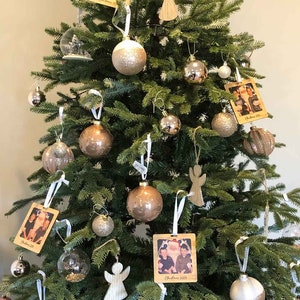 May include: A decorated Christmas tree with ornaments in gold, silver, and white. The tree is decorated with wooden ornaments featuring photos of families and the text "Christmas 2019" and "Christmas 2020".