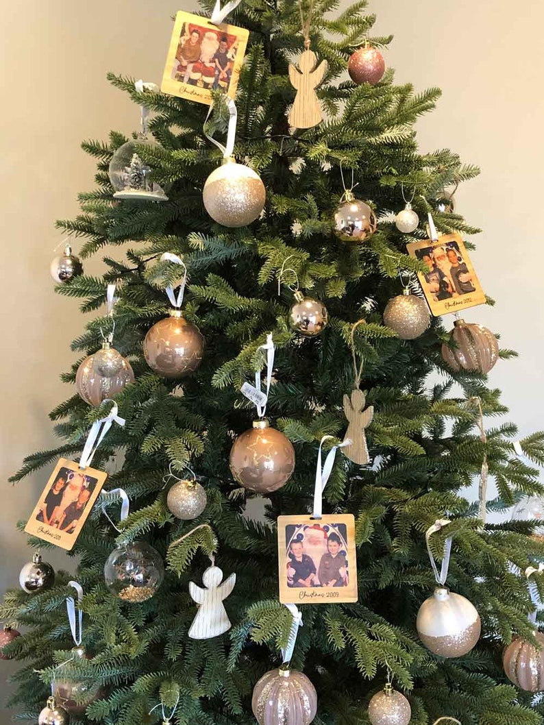 May include: A decorated Christmas tree with ornaments in gold, silver, and white. The tree is decorated with wooden ornaments featuring photos of families and the text "Christmas 2019" and "Christmas 2020".