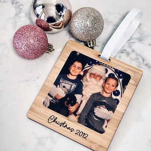 May include: A wooden Christmas ornament with a photo of two children and Santa Claus. The ornament is decorated with the text "Christmas 2012".