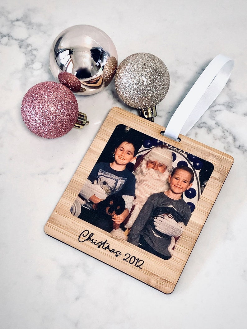 May include: A wooden Christmas ornament with a photo of two children and Santa Claus. The ornament is decorated with the text "Christmas 2012".