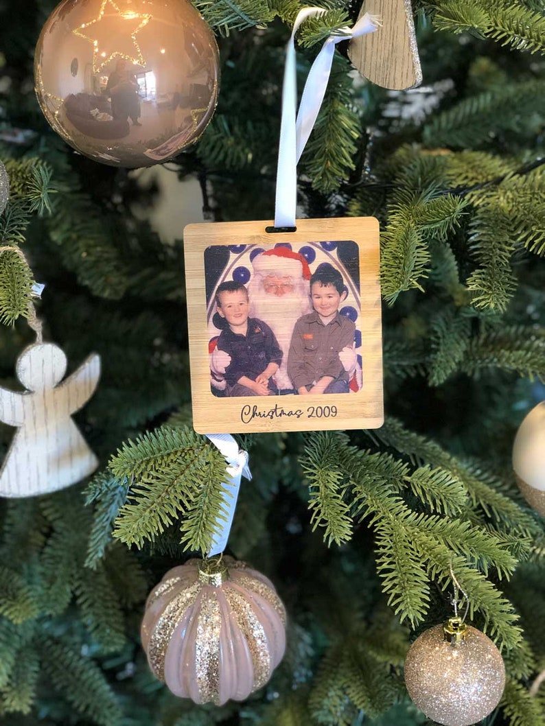 May include: A wooden Christmas ornament with a photo of two children with Santa Claus. The ornament is decorated with the text "Christmas 2009".