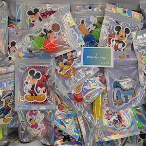 May include: A collection of holographic resealable plastic bags, each featuring a Disney character sticker such as Mickey Mouse, Minnie Mouse, Donald Duck, Daisy Duck, and Pluto. A small rectangular card labeled Pick-See Bags ETS-55 is included.