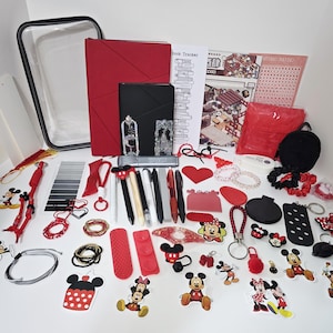 May include: A collection of stationery and accessories including a red notebook, a black notebook, a clear pouch, various pens, stickers featuring Mickey and Minnie Mouse, red and black keychains, hair ties, a mirror, and paper trackers.