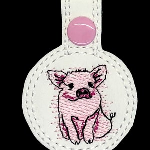 May include: A white fabric key chain with a pink button and a pink embroidered pig.