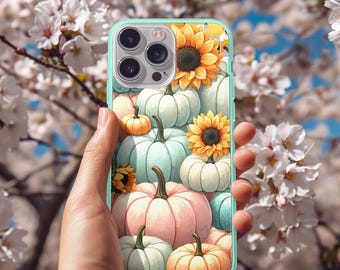 Op de afbeelding: Een mintgroene telefoonhoes met een kleurrijk herfstontwerp. De hoes toont een patroon van pompoenen in verschillende maten en kleuren, waaronder oranje, roze en blauwgroen, samen met zonnebloemen. De achtergrond is een wazige afbeelding van witte bloemen en een blauwe lucht.