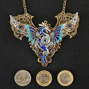 May include: A gold-toned necklace with a blue and green dragon pendant. The dragon is made of metal and has intricate details. The necklace is adorned with blue and clear rhinestones.