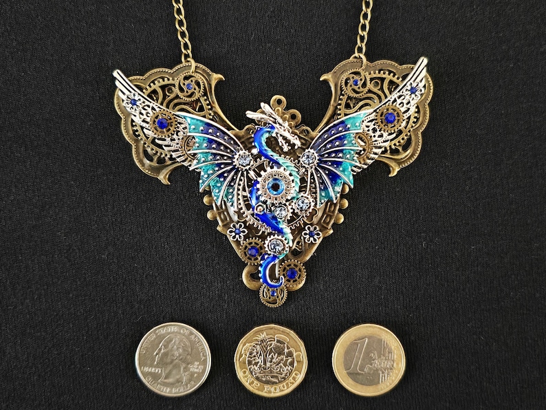 May include: A gold-toned necklace with a blue and green dragon pendant. The dragon is made of metal and has intricate details. The necklace is adorned with blue and clear rhinestones.