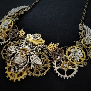 May include: A silver and gold steampunk necklace featuring a bee charm, gears, and floral accents.