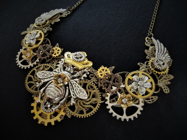 May include: A silver and gold steampunk necklace featuring a bee charm, gears, and floral accents.
