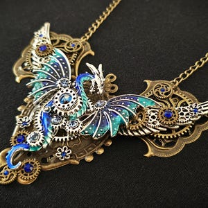 May include: A blue and green dragon pendant necklace with intricate metalwork and blue rhinestones. The dragon is depicted with wings spread and a long tail. The necklace is made of brass and has a steampunk aesthetic.