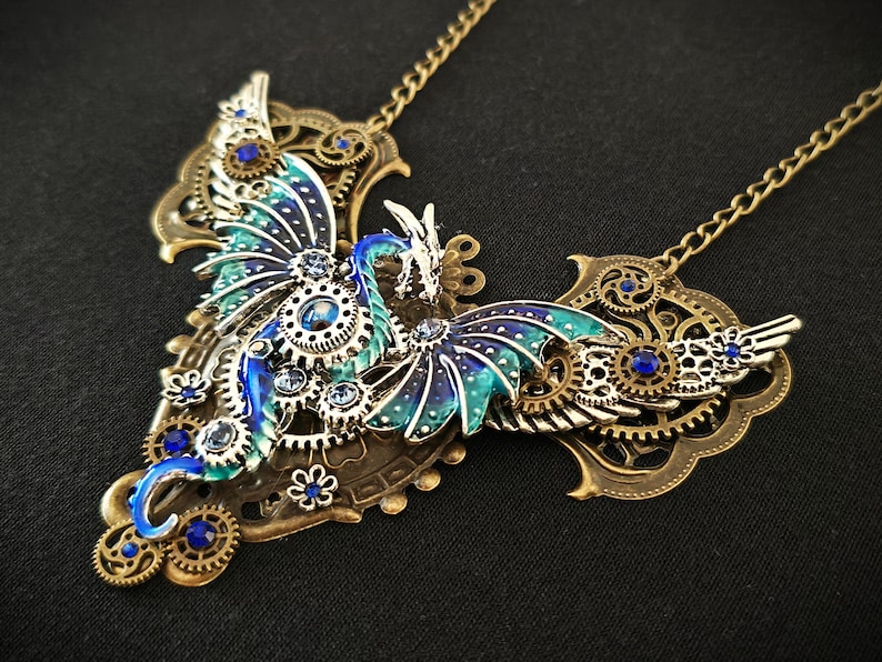 May include: A blue and green dragon pendant necklace with intricate metalwork and blue rhinestones. The dragon is depicted with wings spread and a long tail. The necklace is made of brass and has a steampunk aesthetic.