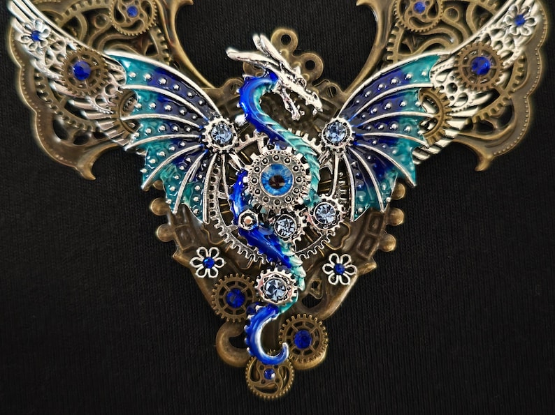 May include: A blue and green dragon with wings made of gears and rhinestones, set against a bronze background. The dragon is a steampunk style pendant.