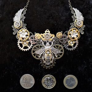 May include: A silver and gold necklace featuring a bee charm and gears. The necklace is made of metal and has a steampunk style.