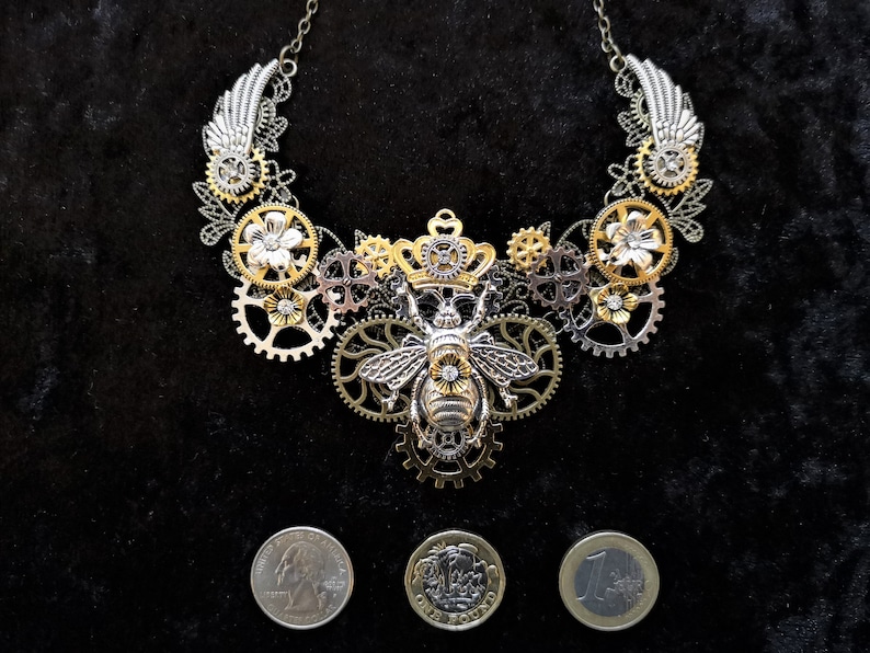 May include: A silver and gold necklace featuring a bee charm and gears. The necklace is made of metal and has a steampunk style.