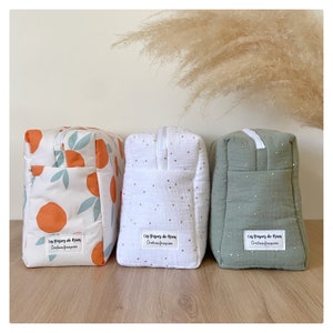 Può includere: Tre pochette in tessuto. La prima ha un motivo di arance e foglie turchesi. La seconda è bianca con pois dorati. La terza è verde salvia con pois dorati. Ogni pochette ha un'etichetta bianca.