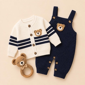 May include: A cream-colored knit cardigan with navy blue stripes and a bear patch, paired with navy blue knit overalls featuring a bear patch and brown buttons, alongside a brown crocheted bear rattle with a wooden ring handle.