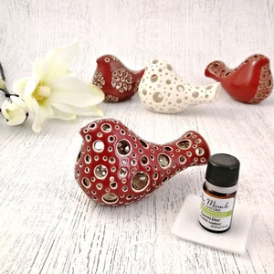 Op de afbeelding: Vier keramische vogelbeeldjes, twee rood en twee wit, met een decoratief uitgesneden ontwerp. De vogels zijn gerangschikt op een wit houten oppervlak. Een klein flesje etherische olie en een wit wattenstaafje zijn ook zichtbaar.