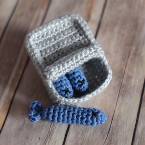 May include: A handmade crochet baby gift set featuring a gray carrier with two blue booties and a blue fish-shaped toy. The set is made of soft yarn and is designed for newborns. The booties and fish toy are approximately 4 inches long.