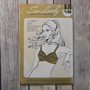 May include: Vintage "Sew Lovely" lingerie pattern featuring a line drawing of a woman wearing a bra. The pattern includes sizes 32, 34, and 36, with A, B, and C cup sizes. The cover is tan and gold with the price tag of $1.00.