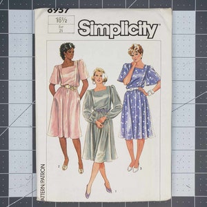May include: Simplicity sewing pattern with three dress designs. The pattern includes a pink dress, a grey dress, and a blue dress with white polka dots. The pattern number is 6957, with a size of 16 1/2 and Eur 21.