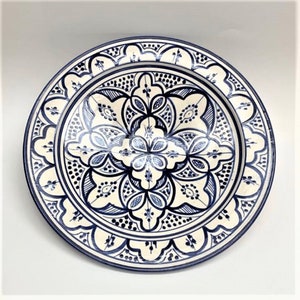 Peut inclure: Une assiette en céramique blanche avec un motif floral bleu et blanc complexe. L'assiette a un bord surélevé et une surface lisse.