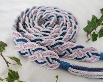 Op de afbeelding: Een gevlochten koord van roze, grijs en blauw katoenen garen. Het koord is opgerold en heeft een decoratief knoopje aan het einde.