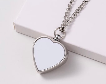 May include: A silver heart-shaped pendant necklace with a white, blank surface. The pendant is attached to a silver chain.