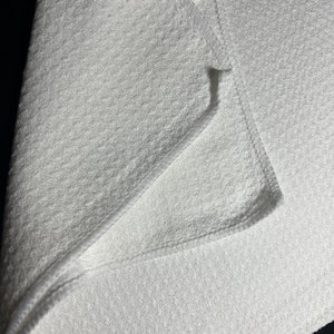 Puede incluir: Un paño de microfibra blanco para limpiar, doblado por la mitad, que muestra la textura suave y los bordes cosidos.